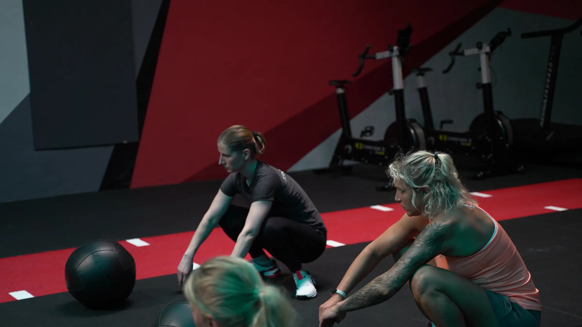 Drei Frauen in der Hocke am Medizinball vor den Ausdauergeräten im Iron Gym Viersen