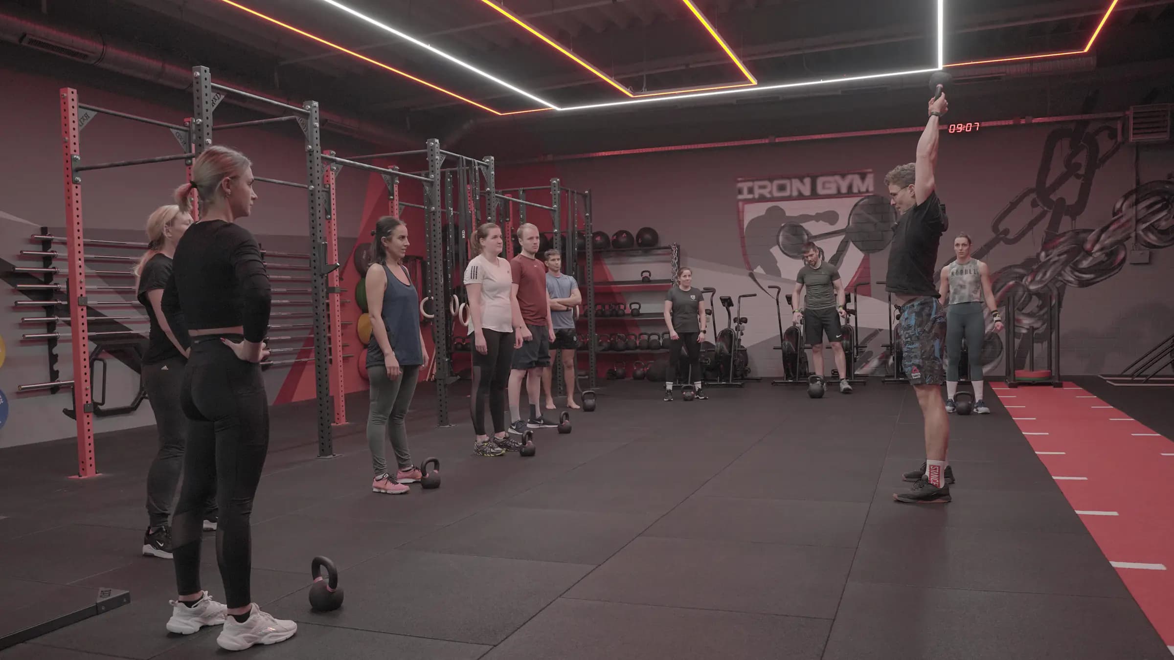 Athletics-Kurs im Iron Gym Viersen: Eine Gruppe steht mit Kettlebells bereit, der Trainer stemmt vorne rechts eine Hantel über Kopf