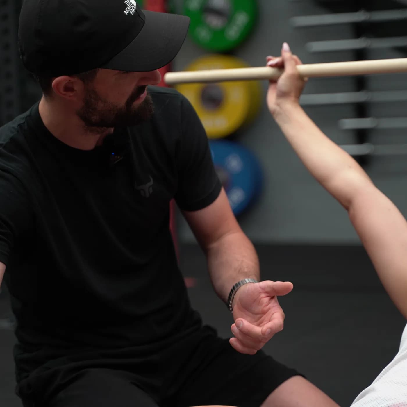 Trainer erklärt einer Teilnehmerin die Überkopf-Position mit dem Holzstab im Athletic Basics Kurs im Iron Gym Viersen