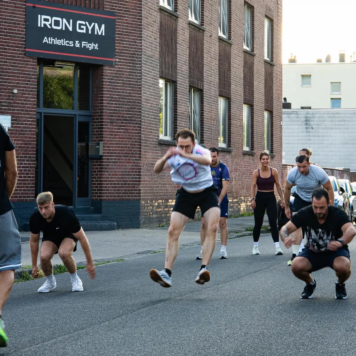 Sportler springt vor dem Iron Gym Viersen aus dem Stand nach vorn, die Gruppe geht daneben in die Hocke für den nächsten Sprung