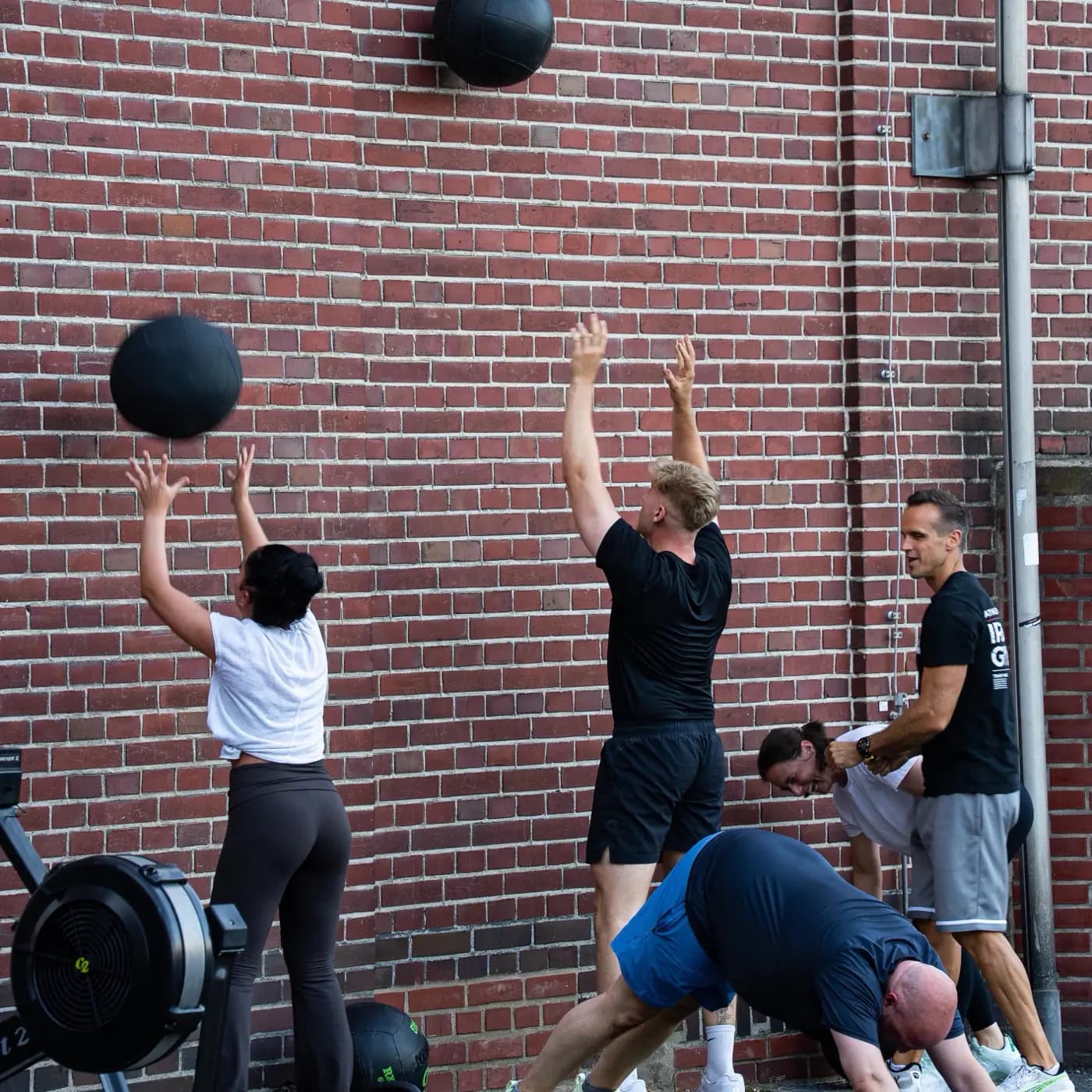 Zwei Wall Balls fliegen gegen die Backsteinwand des Iron Gym Viersen, die Werfer stehen mit gestreckten Armen darunter