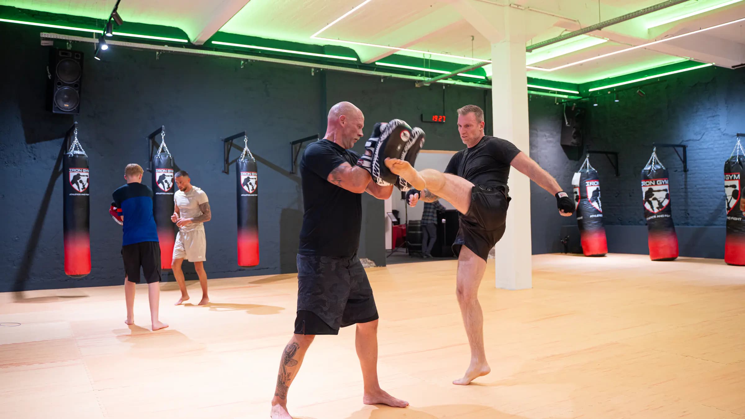 Kampfsporttraining im Iron Gym: Ein Sportler tritt gegen die Pratze seines Trainingspartners, im Hintergrund weitere Trainierende an den Sandsäcken