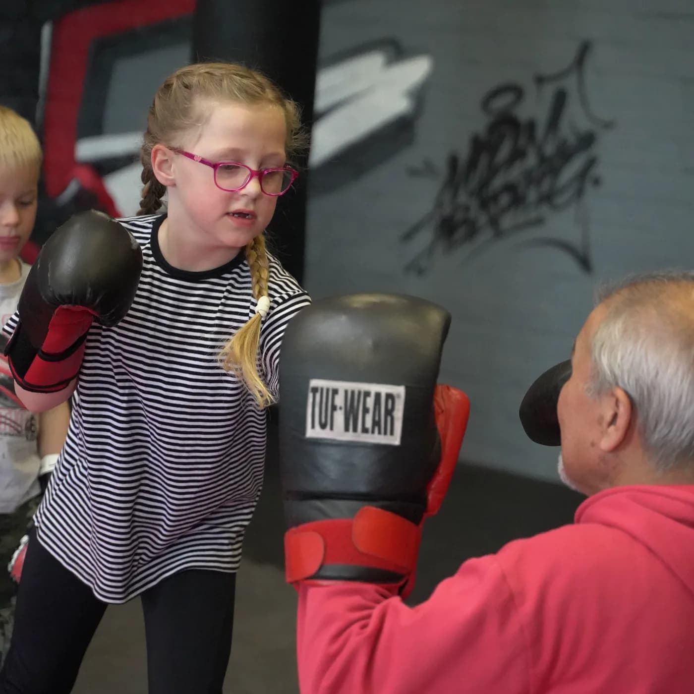 Kinder-Kampfsport im Iron Gym Viersen: Ein Mädchen schlägt konzentriert in die Pratze des Trainers
