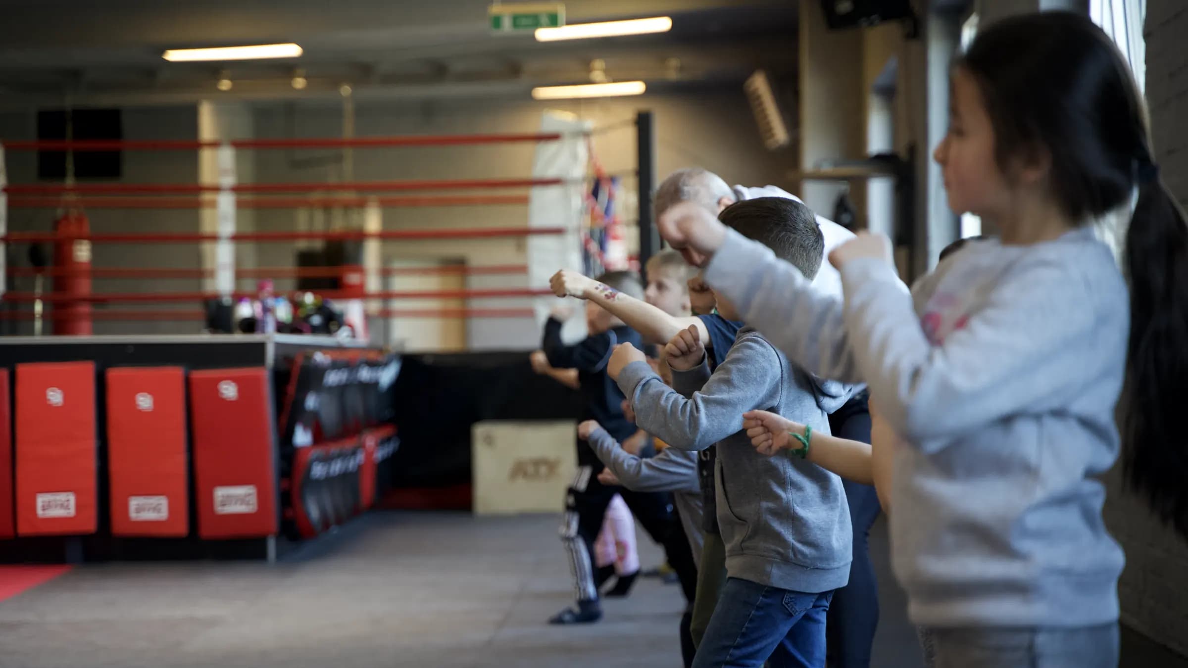 Bambini-Gruppe im Iron Gym Viersen steht in einer Reihe und schlägt gemeinsam eine Gerade, im Hintergrund der Boxring