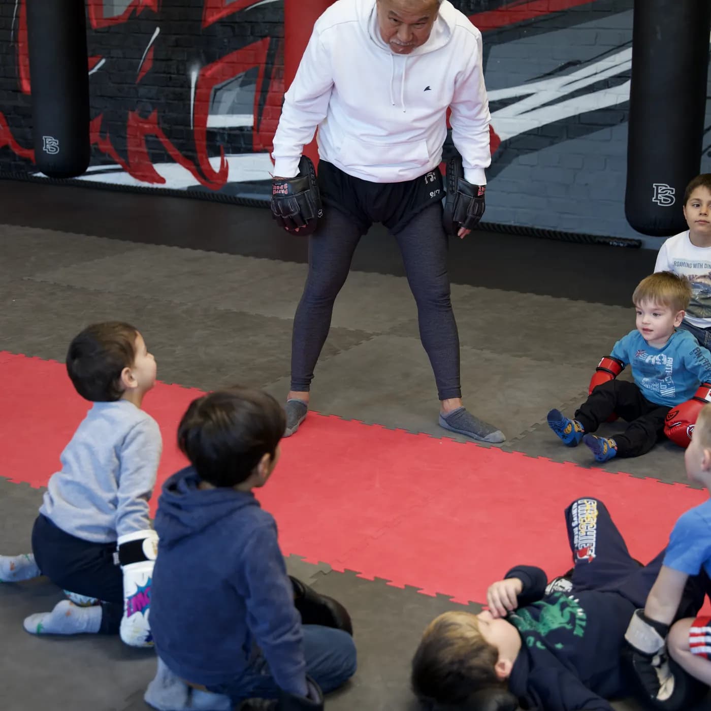 Bambini-Gruppe sitzt und liegt auf der Mattenfläche um den Trainer im Iron Gym Viersen
