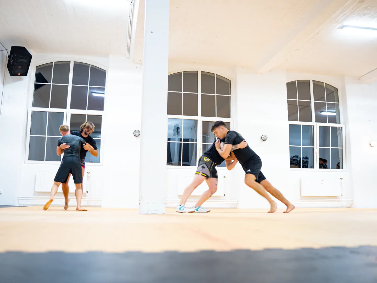 Zwei Trainingspaare üben Ringen und Takedowns im Stand auf der Matte des Iron Gym